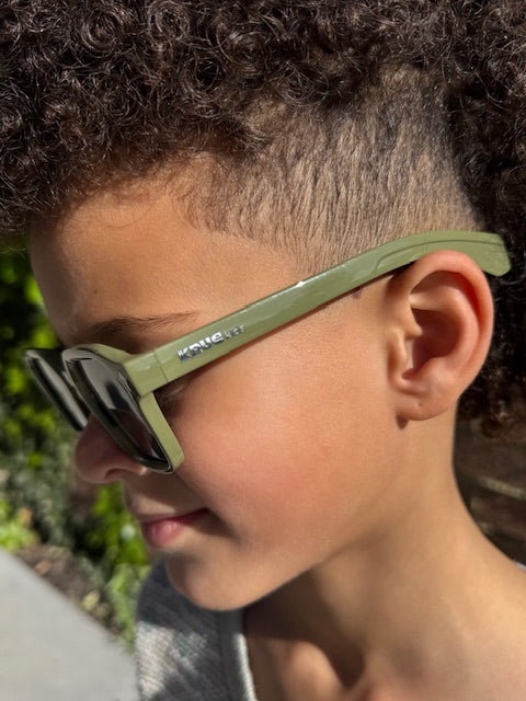 Close-up of a child wearing green sunglasses with a blurred natural background