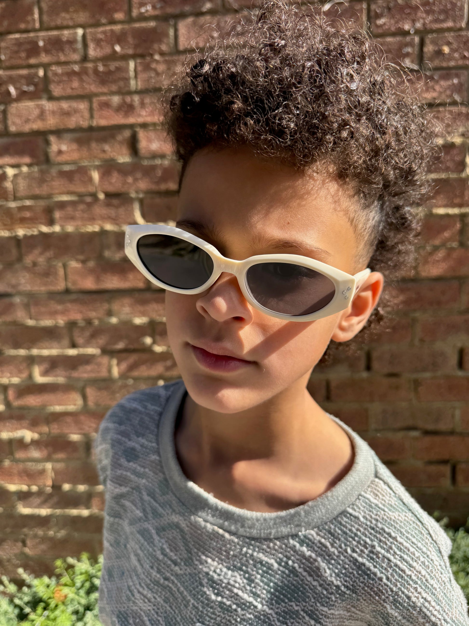 Person wearing white sunglasses with a brick wall background